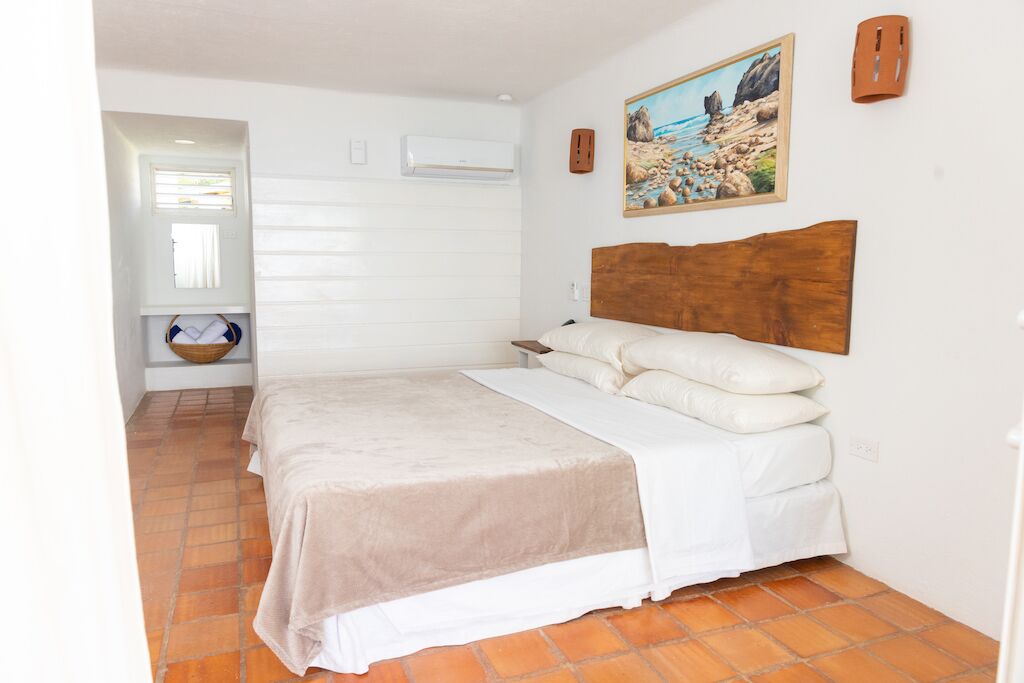 A bedroom with a large bed, a wooden headboard, a painting on the wall, and a window with blinds.