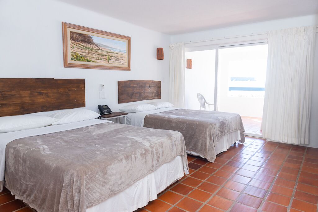A hotel room with two beds, a painting on the wall, a phone on the nightstand, and a view of the outside through a sliding door.