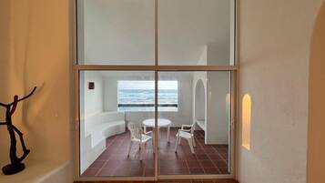 A room with a sliding glass door leading to an outdoor seating area with a view of the sea.