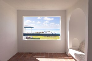 A room with a large window overlooking a beach with lounge chairs and a pool. - OceanBlue (Inch Marlowe)