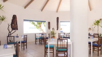 A restaurant with multiple tables and chairs, wooden beams on the ceiling, and decorative wall art.