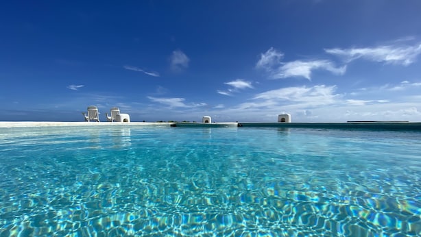 A clear blue pool with a view of the ocean and white structures in the background. - OceanBlue (Inch Marlowe)