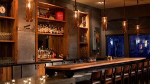 A bar area with a long counter, wooden shelves with bottles, and hanging light fixtures.