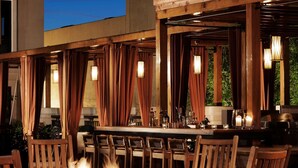 An outdoor seating area with a fire pit, wooden chairs, and a bar with a view of the sky.