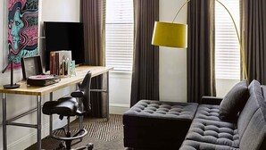 Ein modernes Hotelzimmer mit einer schwarzen Ledersofa, einem Schreibtisch mit Computer, einem großen Gemälde an der Wand und einer Stehlampe.