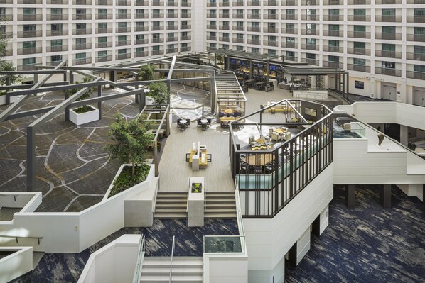 A modern hotel atrium with multiple levels, outdoor seating areas, and a central staircase.