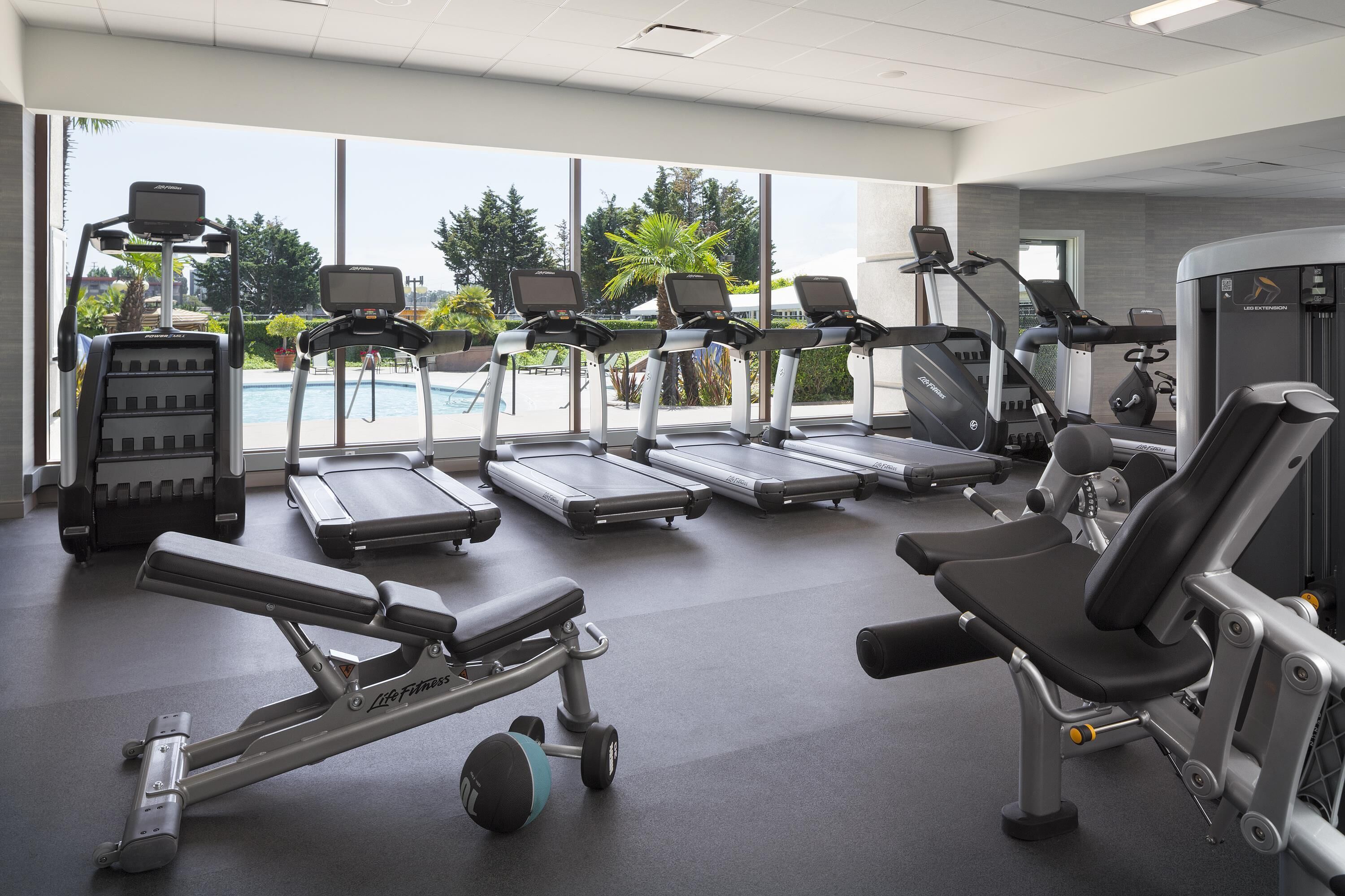 Ein Fitnessstudio mit Laufbändern, Crosstrainern und Gewichtsbänken.