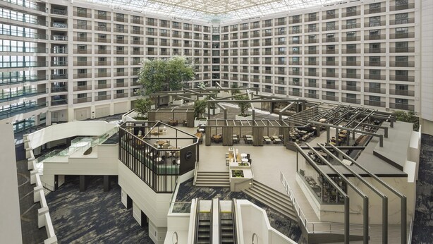 A modern hotel atrium with multiple floors, a central staircase, and a variety of seating areas.