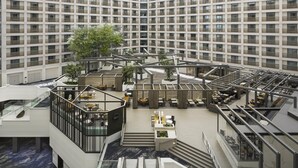 A modern hotel atrium with a central open space, multiple floors, and a glass ceiling.