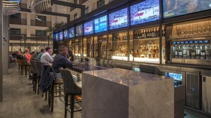A bar area with multiple screens displaying sports events, a variety of liquor bottles, and seating for guests.