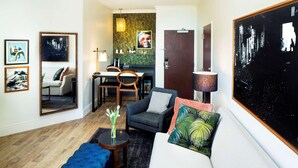 A modern living room with a sofa, armchair, and ottoman, a dining area with a table and chairs, and a kitchen visible through an open door. - 2 Connecting Suites at a 4⭐️ Hotel (Savannah)