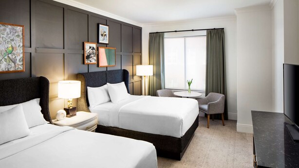 A hotel room with two beds, a desk, a chair, a TV, and artwork on the walls. - 2 Connecting Suites at a 4⭐️ Hotel (Savannah)