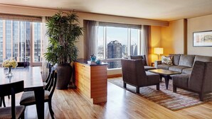 A modern hotel room with a dining area, a sofa set, a large potted plant, and a city view through the windows. - 2 Connecting Suites at a 4.5⭐️ Hotel (Seattle)