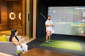 Ein Zimmer mit einer grünen Matte, einem Dartboard und einem Bildschirm, der ein Golfspiel zeigt.