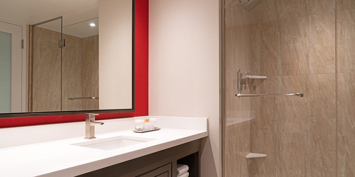 A modern bathroom with a white sink, a large mirror, and a shower area.