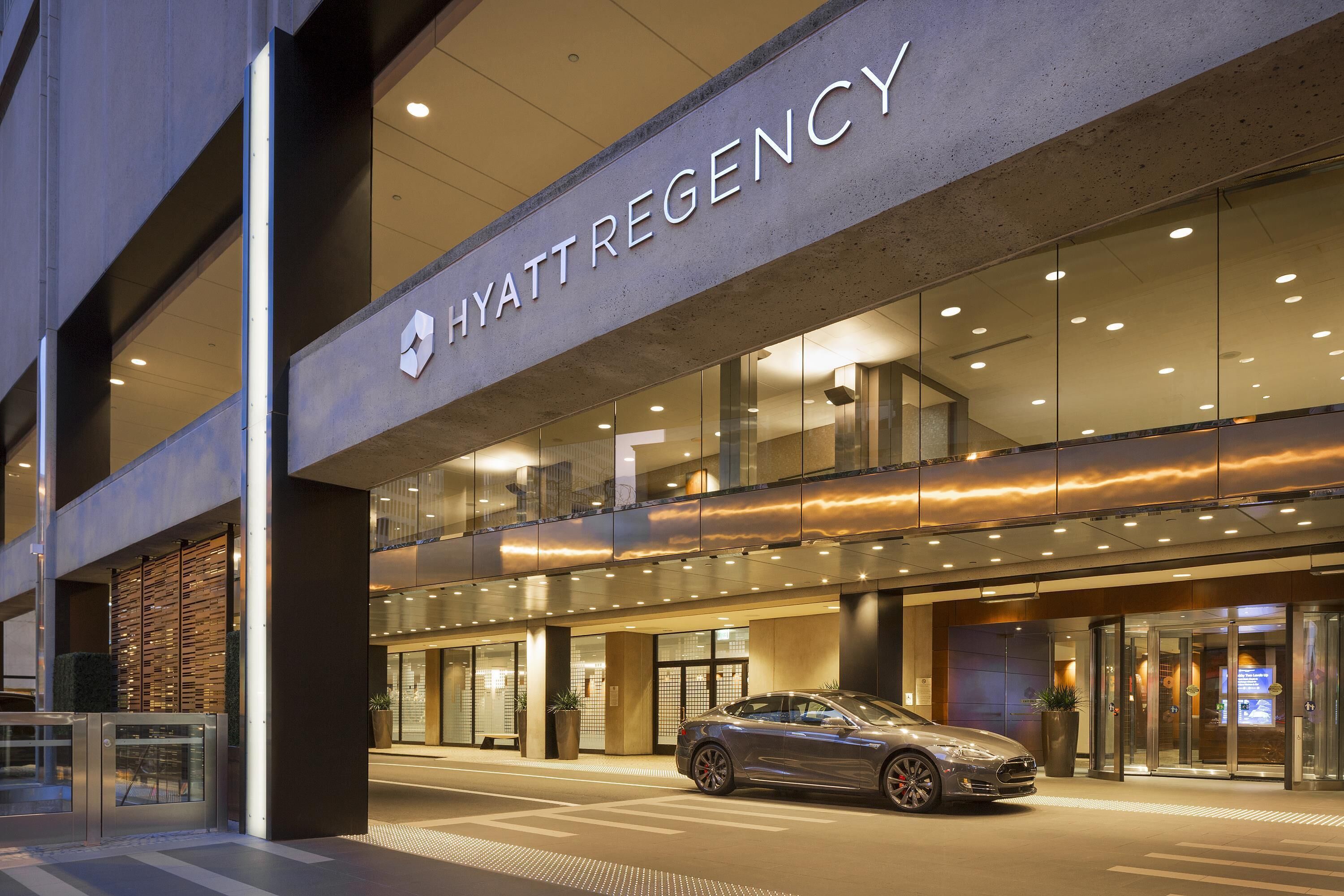 A modern hotel entrance with a car parked in front, glass doors, and a sign reading 'HYATTREGENCY'.