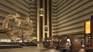 A spacious lobby with a large abstract sculpture, tiered seating, and modern lighting fixtures.