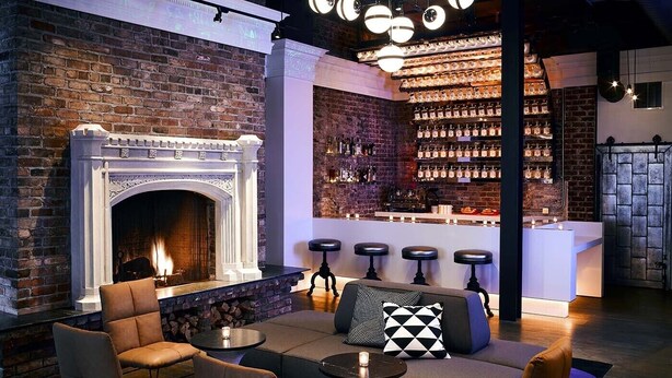 A cozy lounge area with a fireplace, leather seating, a bar with shelves of bottles, and a modern design.