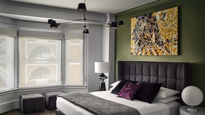 A modern bedroom with a large bed, a window with a view, and a unique abstract painting on the wall.