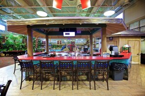 Un espace bar intérieur avec un comptoir, des tabourets de bar et une vue sur la piscine.