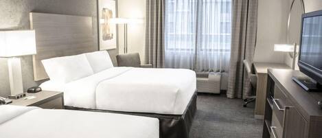 A hotel room with two beds, a desk, a television, and a large window with curtains.