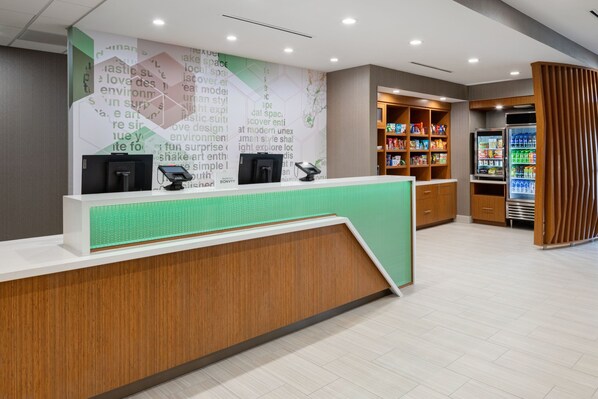 A reception area with a wooden counter, a green-tiled wall, and a refrigerator stocked with beverages. - SpringHill Suites by Marriott Weatherford Willow Park (Weatherford)