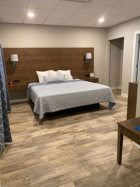 A hotel room with a bed, wooden headboard, bedside lamps, a nightstand, a wooden floor, and a door.