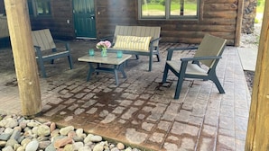 A wooden cabin with a covered patio, outdoor seating, and a view of the surrounding landscape.