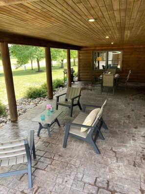 Eine Terrasse im Freien mit Steinböden, Holzbalken und Sitzgelegenheiten, darunter Stühle und ein Tisch.