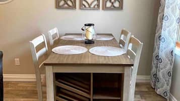 Une table à manger avec six chaises, une machine à café, des éléments décoratifs muraux et un rideau à motifs.