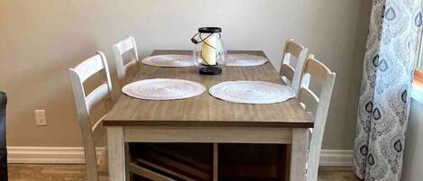 A dining table with six chairs, a coffee maker, decorative wall art, and a patterned curtain.