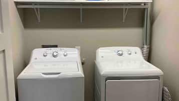 Une buanderie équipée de deux machines à laver à chargement frontal, d’un étendoir et d’une étagère contenant des produits de lessive.