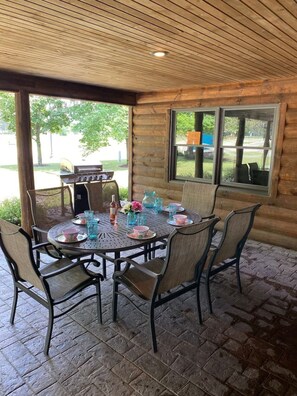A covered patio with a round table and chairs, a grill, and a view of the outdoors. - Alpine Lodge-Rome Away From Home-5min Sand Valley (Nekoosa)