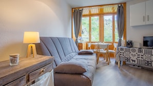 A cozy room with a sofa, a small table with a lamp, a coffee machine, and a view of greenery outside. - L'Eclose - Studio au pied des pistes - Alpe d'Huez (Huez)