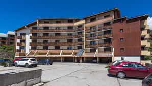 A multi-story building with balconies, a parking area, and a clear blue sky. - L'Eclose - Studio au pied des pistes - Alpe d'Huez (Huez)