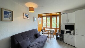 A modern living room with a dark-colored sofa, a dining table with chairs, and a kitchen area with cabinets and appliances. - L'Eclose - Studio au pied des pistes - Alpe d'Huez (Huez)