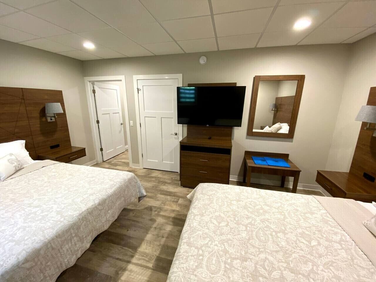 A hotel room with two beds, a TV, a mirror, a desk, and a wardrobe.
