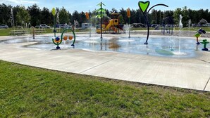 A water play area with multiple fountains and a playground in the background.