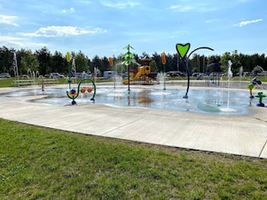 A water play area with multiple fountains and a playground in the background. - Fairway Lodge-Rome Away From Home-5min Sand Valley (Nekoosa)