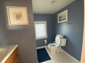 Ein Badezimmer mit Toilette, Waschbecken, einem Fenster mit Jalousien und einem gerahmten Bild an der Wand.