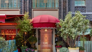 A hotel entrance with a red awning, potted plants, and a brick facade. - Broadwick Soho (London)