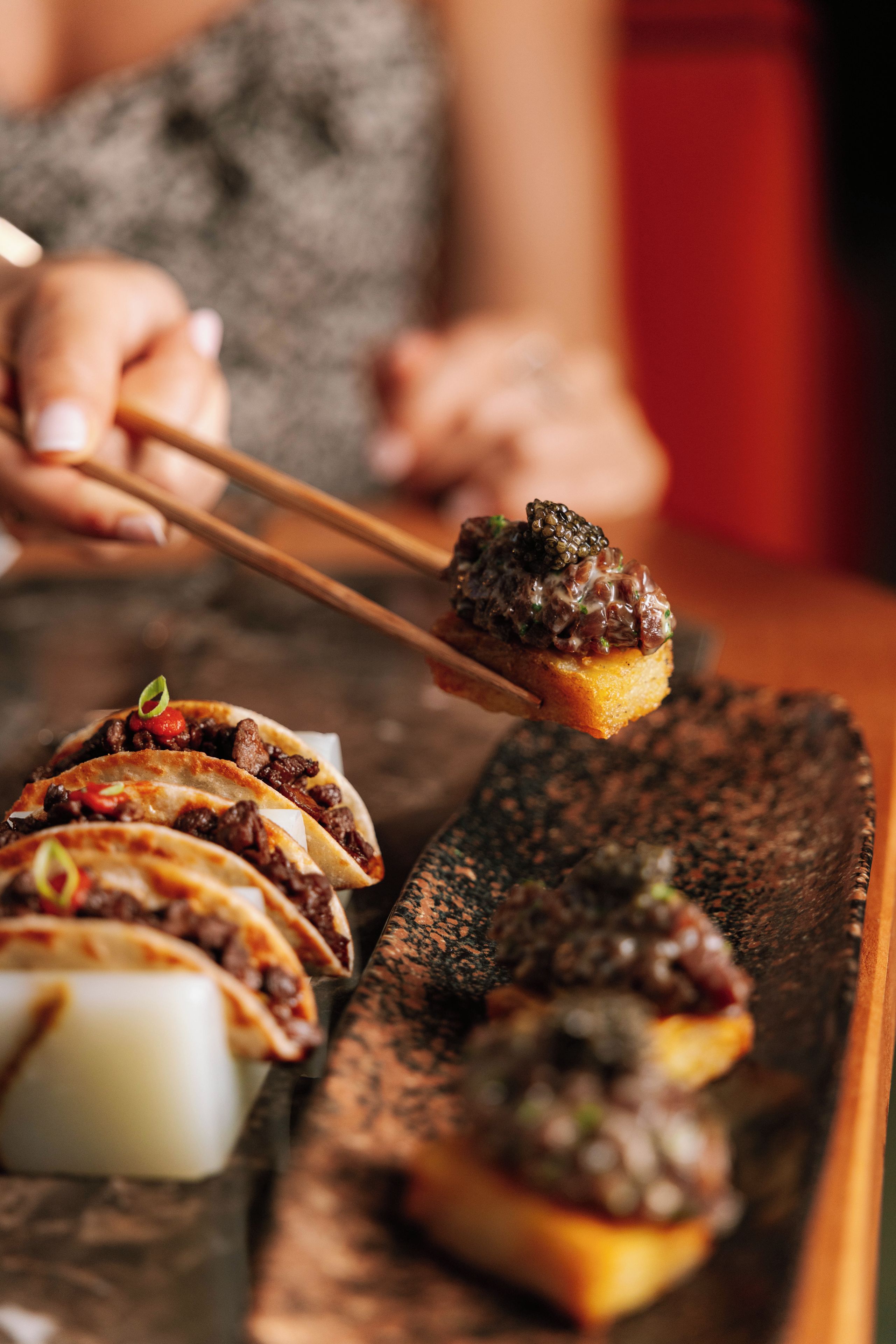 A person holding a piece of food with chopsticks.