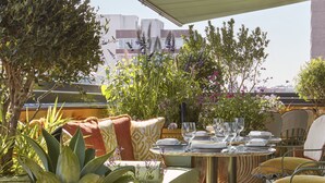Un espace de restauration en plein air avec une table ronde pour deux personnes, entourée de sièges confortables et de différentes plantes.