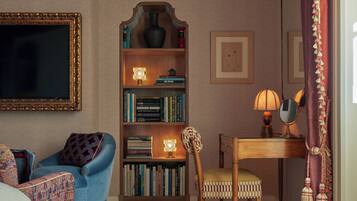 A cozy room with a blue armchair, a wooden chair, a bookshelf, and a desk with a lamp.