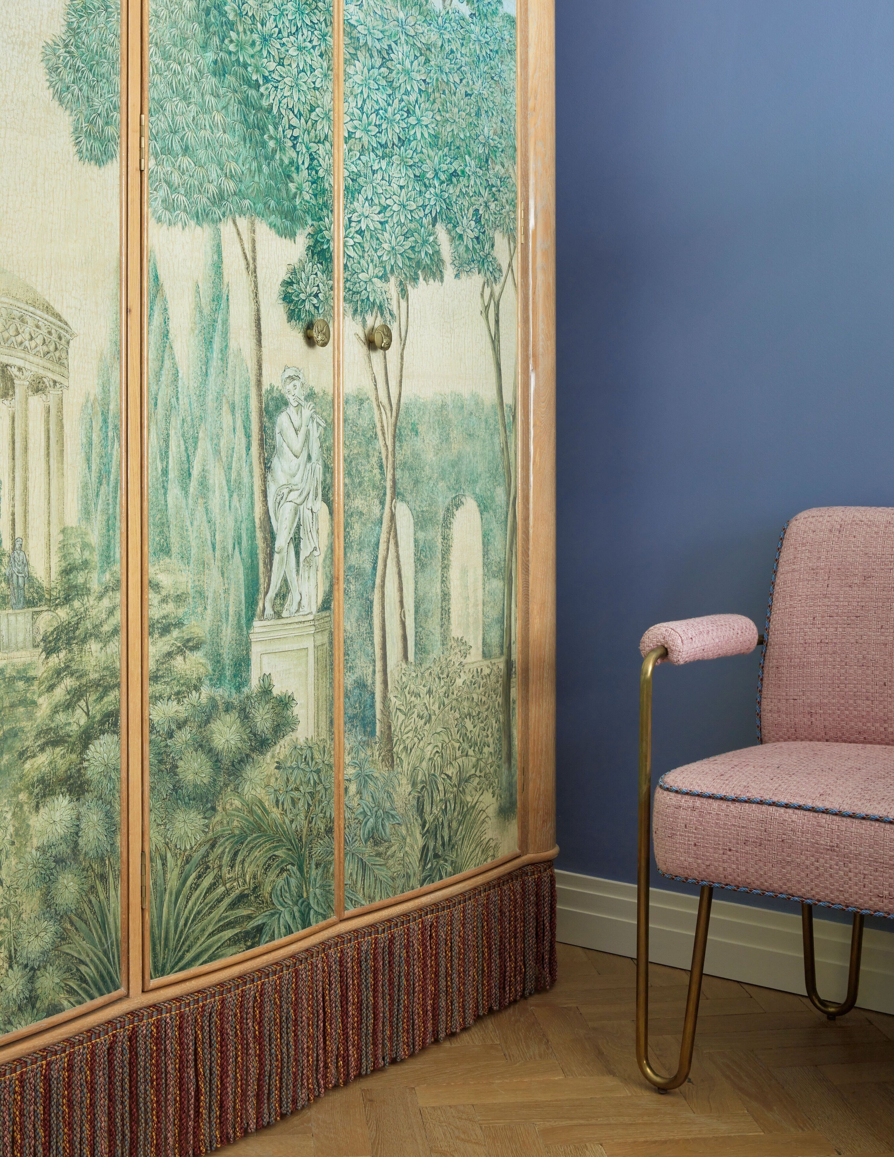 A room with a large tapestry depicting a garden scene, a pink chair, and a blue wall.