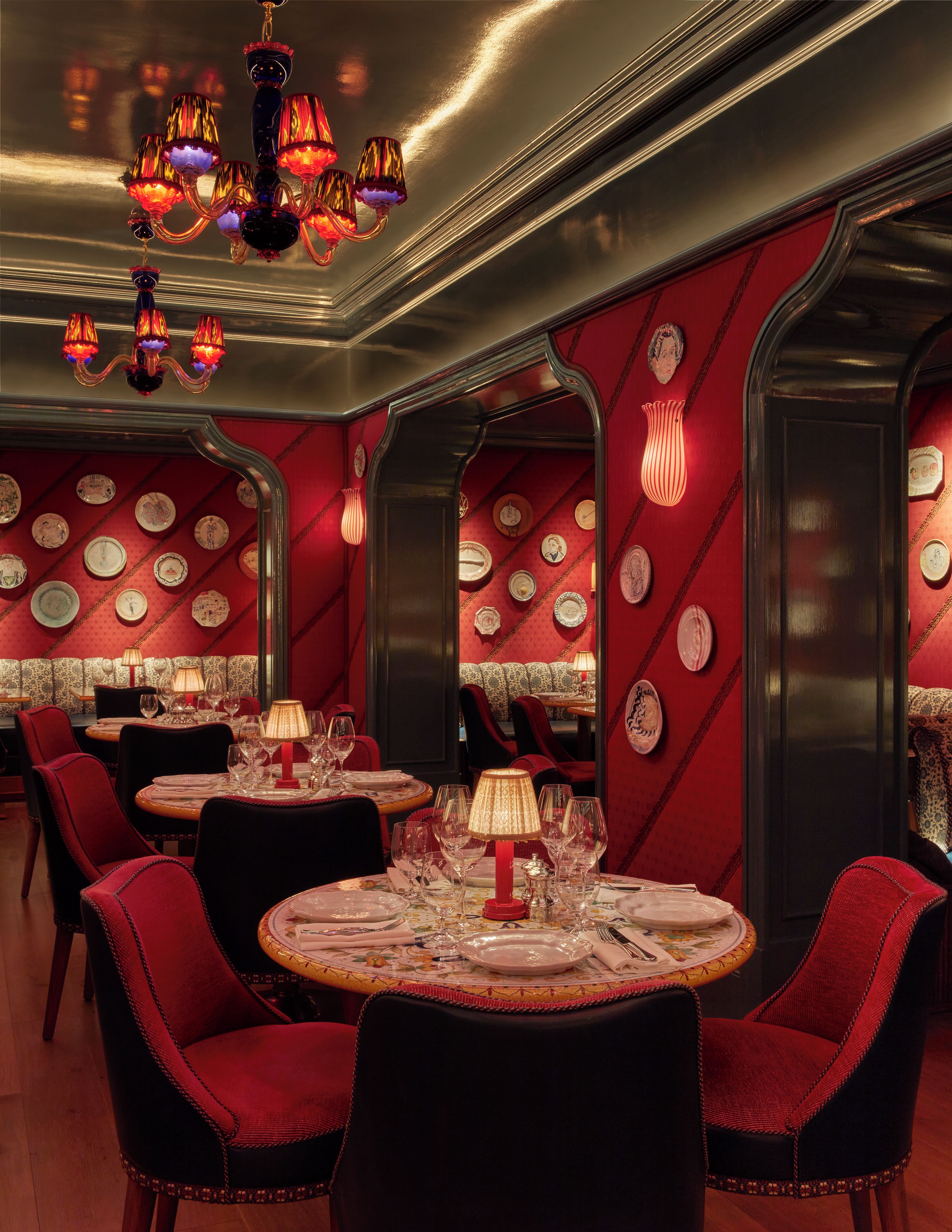 A restaurant interior with round tables, red upholstered chairs, and a chandelier.
