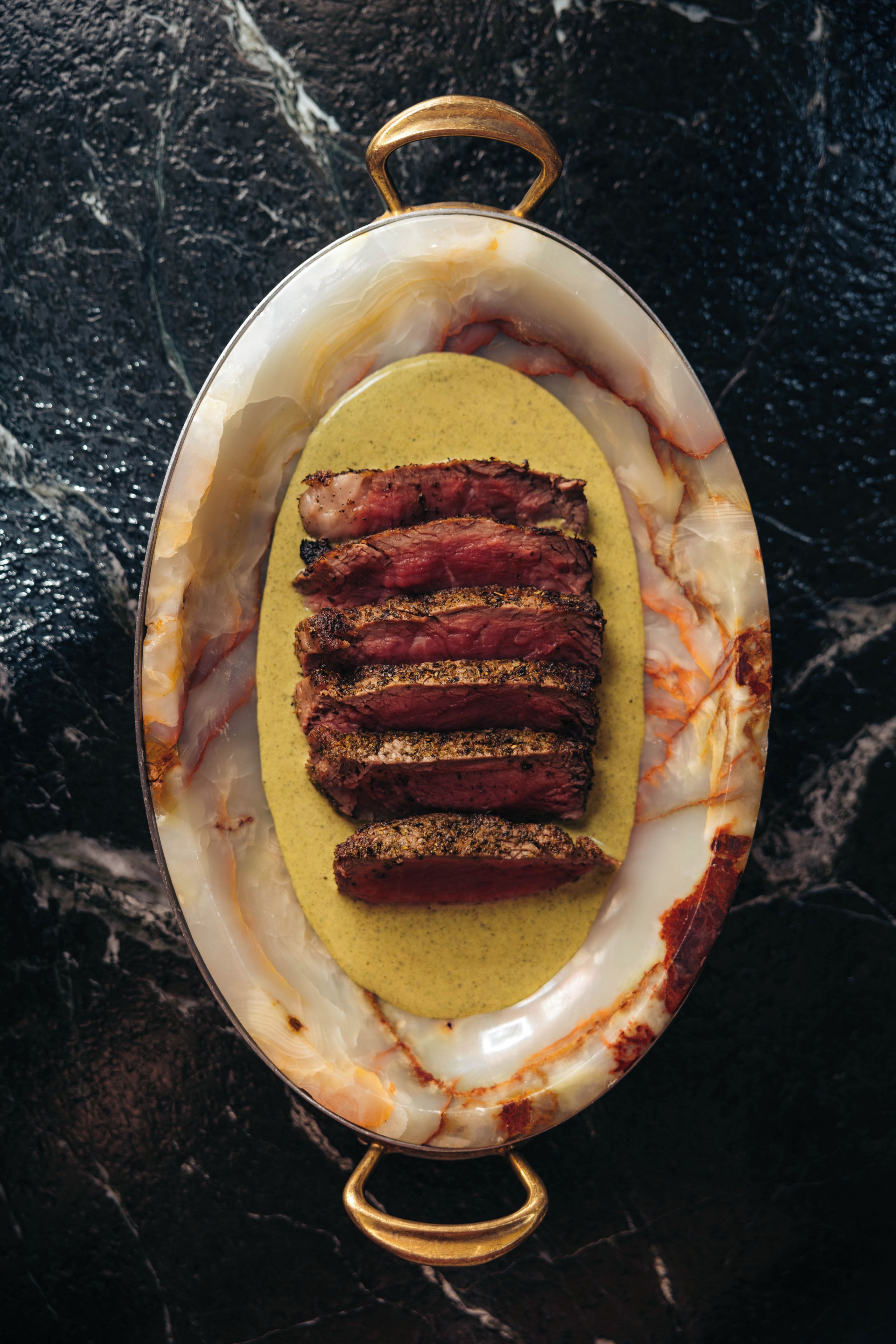 A dish with sliced meat and a yellow sauce in a ceramic dish with handles.