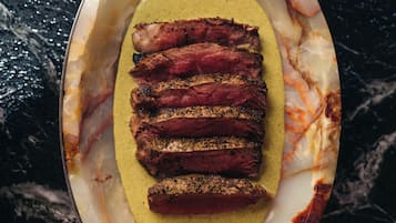 A dish with sliced meat and a yellow sauce in a ceramic dish with handles.