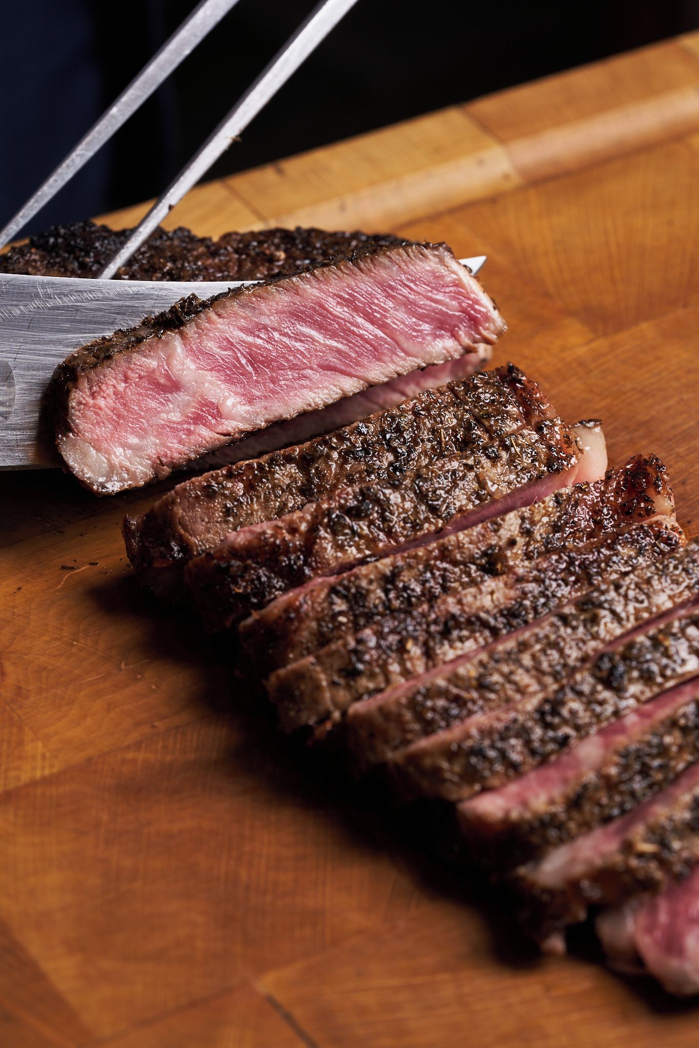 A steak with a pink center and charred exterior, sliced on a wooden cutting board.