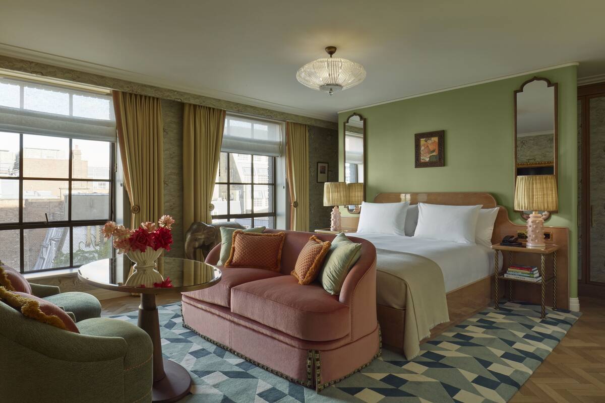 Una habitación de hotel con una cama grande, una zona de estar con sofá y mesa, un espejo y vistas de la ciudad desde la ventana.